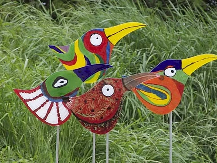 Drie vrolijke vogels van glas op standaards in het gras